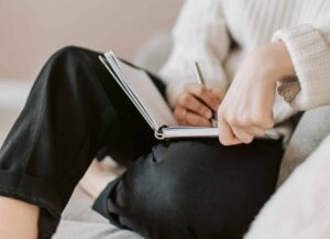 Close-up of person writing in a notebook on their lap.