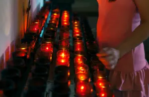 Rows of candles lit in votive holders with person lighting one