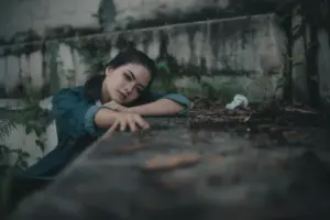 Young woman with head resting on outdoor bench, looking sad.