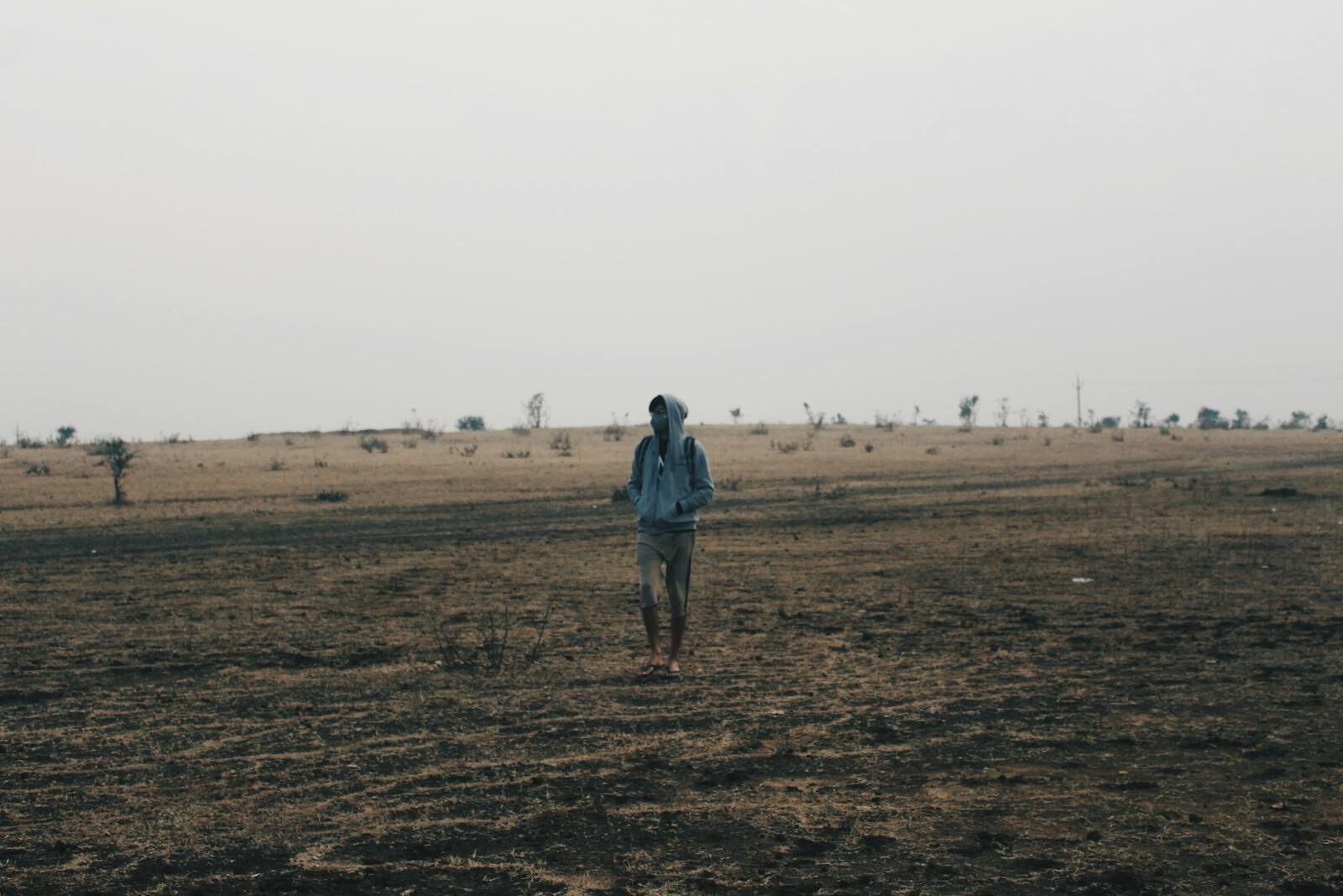 A lone person in a hoodie walks across a barren wasteland, evoking solitude.